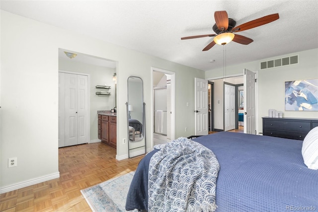 bedroom with visible vents, ensuite bathroom, a ceiling fan, a textured ceiling, and baseboards