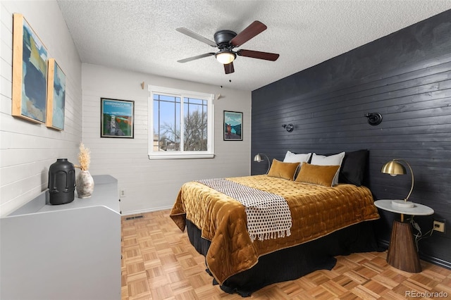 bedroom featuring a ceiling fan, visible vents, wood walls, and a textured ceiling