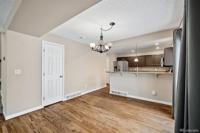 kitchen featuring light hardwood / wood-style flooring, a breakfast bar, appliances with stainless steel finishes, dark brown cabinets, and kitchen peninsula