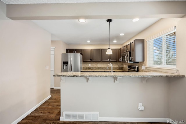 kitchen featuring hanging light fixtures, stainless steel appliances, a breakfast bar, and kitchen peninsula