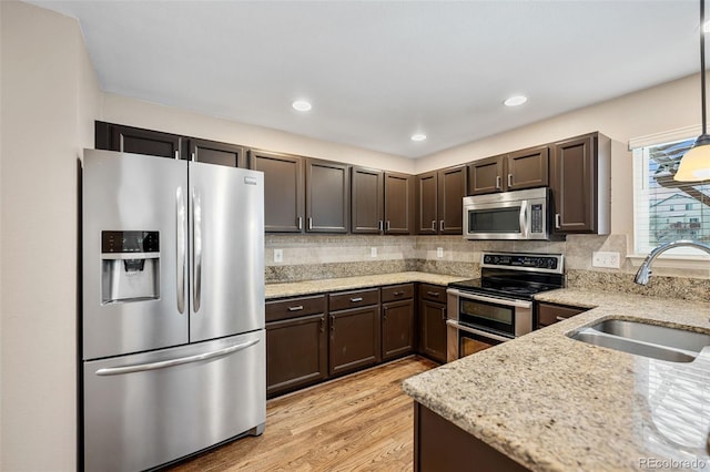 kitchen with appliances with stainless steel finishes, pendant lighting, sink, dark brown cabinetry, and light stone counters