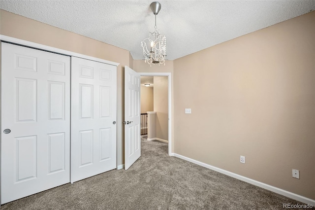 unfurnished bedroom with carpet floors, an inviting chandelier, a textured ceiling, and a closet