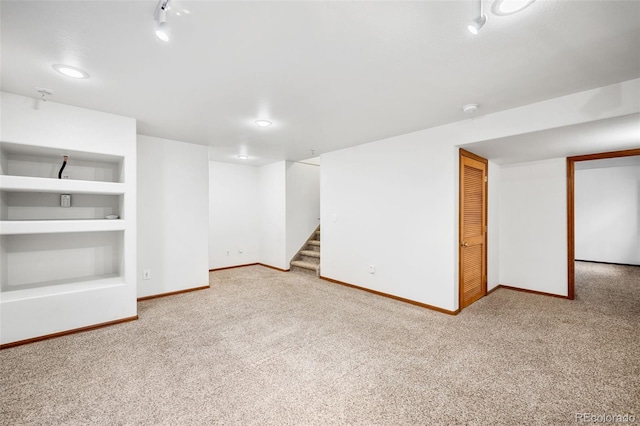 basement featuring track lighting, built in features, and carpet