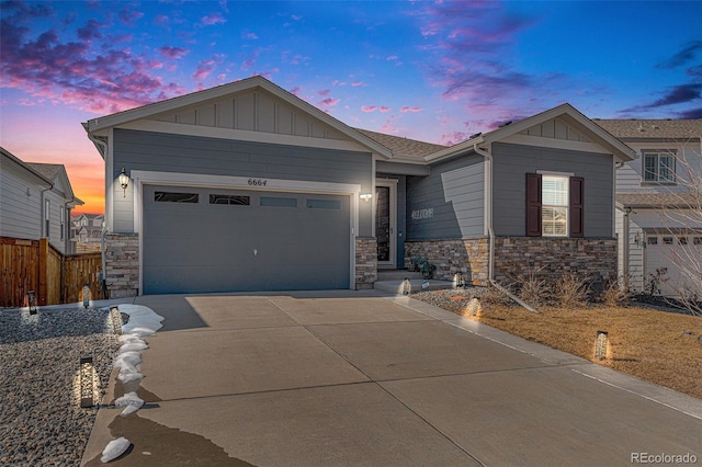 view of front of home with concrete driveway, board and batten siding, stone siding, an attached garage, and fence