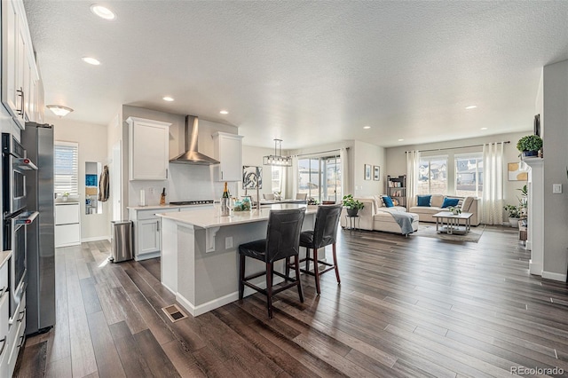 kitchen featuring dark wood-style flooring, wall chimney range hood, open floor plan, white cabinetry, and light countertops