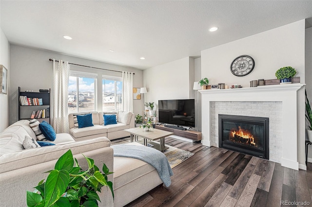 living area featuring baseboards, a brick fireplace, a textured ceiling, recessed lighting, and dark wood-type flooring