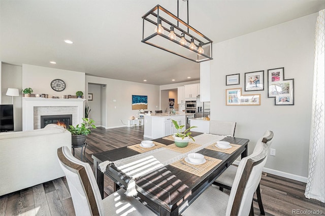 dining space featuring dark wood-style flooring, baseboards, a glass covered fireplace, and recessed lighting