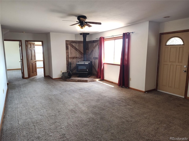 unfurnished living room featuring ceiling fan, dark colored carpet, a healthy amount of sunlight, and a wood stove