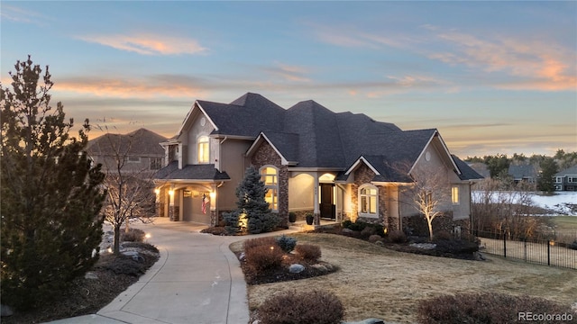 french country style house with stone siding, curved driveway, stucco siding, and fence