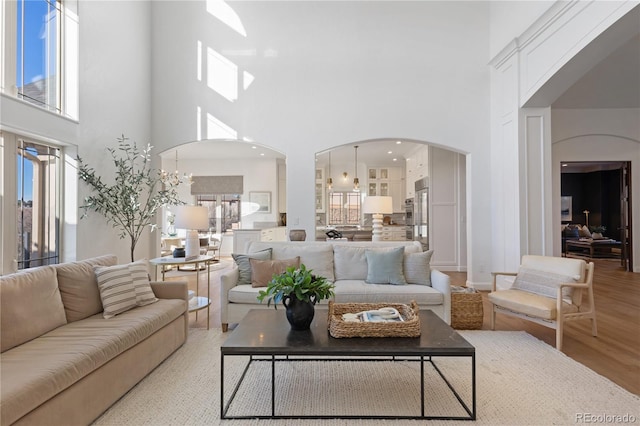 living area featuring arched walkways, a notable chandelier, a high ceiling, and light wood finished floors