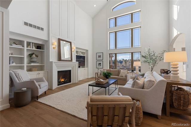 living room with visible vents, a warm lit fireplace, wood finished floors, arched walkways, and high vaulted ceiling