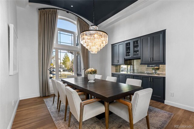 dining room featuring a notable chandelier, wood finished floors, baseboards, and a towering ceiling