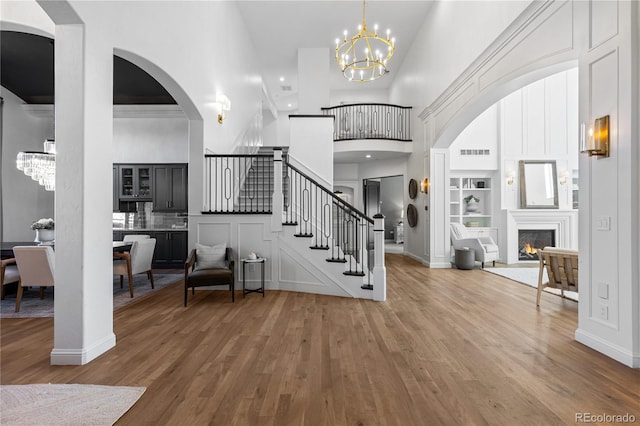 entrance foyer featuring visible vents, a warm lit fireplace, wood finished floors, stairway, and a chandelier