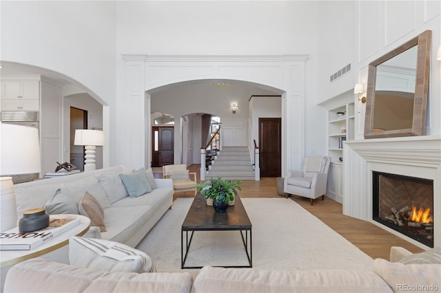 living room with arched walkways, visible vents, a towering ceiling, and a lit fireplace