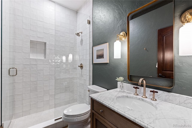 full bathroom with vanity, toilet, a shower stall, and a textured wall