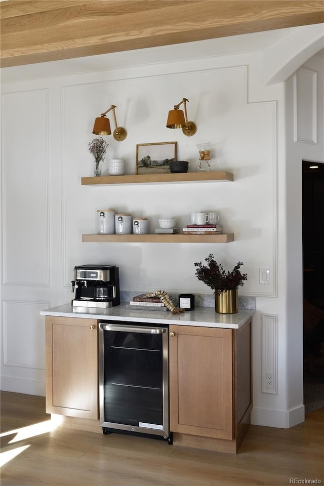 bar with light wood-style flooring, wine cooler, a dry bar, and a decorative wall