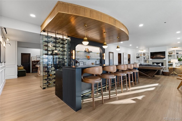 bar featuring light wood finished floors, decorative backsplash, recessed lighting, a fireplace, and wet bar