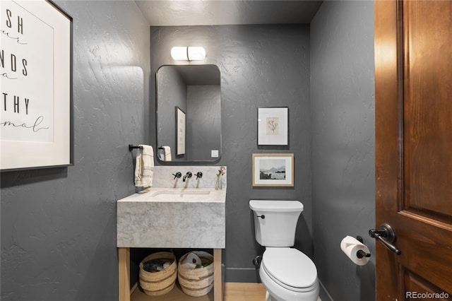 half bath featuring toilet, vanity, and a textured wall