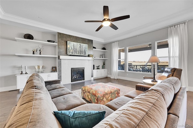 living area with a large fireplace, baseboards, ornamental molding, and wood finished floors