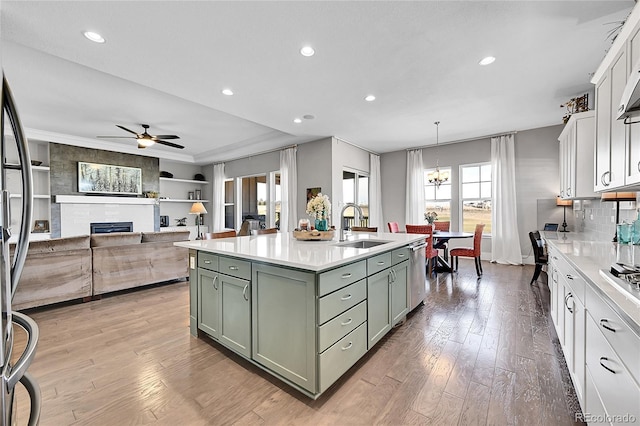 kitchen with a fireplace, light wood-style flooring, a sink, green cabinetry, and dishwasher