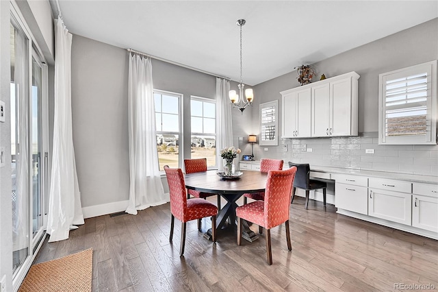 dining space with built in desk, an inviting chandelier, baseboards, and dark wood-type flooring