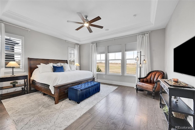 bedroom featuring baseboards, a raised ceiling, ceiling fan, ornamental molding, and wood finished floors