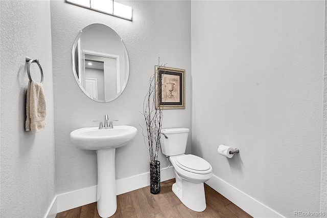 half bath featuring baseboards, a sink, toilet, and wood finished floors