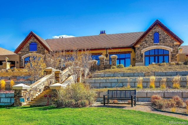 rear view of house featuring stone siding, stairway, and a lawn