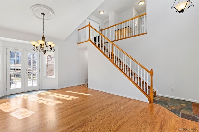 interior space featuring an inviting chandelier, a towering ceiling, wood-type flooring, and french doors