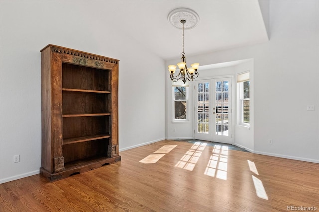 unfurnished dining area featuring lofted ceiling, a chandelier, light wood-type flooring, and french doors