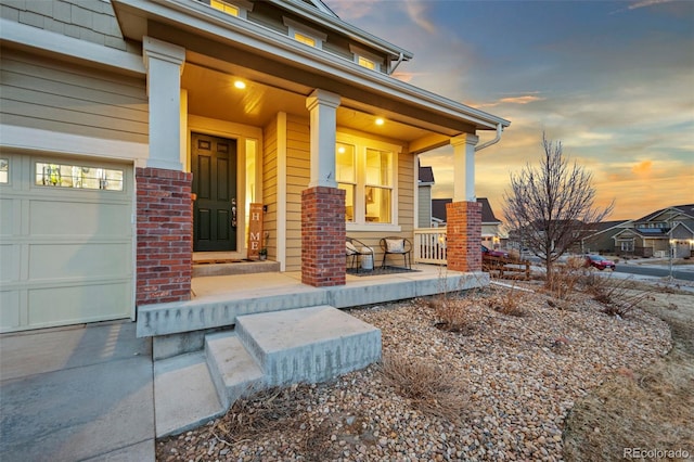 exterior entry at dusk with a porch, brick siding, and an attached garage