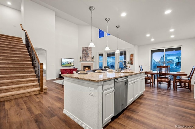 kitchen with dark wood-style flooring, light stone countertops, a kitchen island with sink, white cabinetry, and stainless steel dishwasher