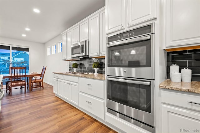 kitchen with appliances with stainless steel finishes, light wood-type flooring, white cabinets, and tasteful backsplash