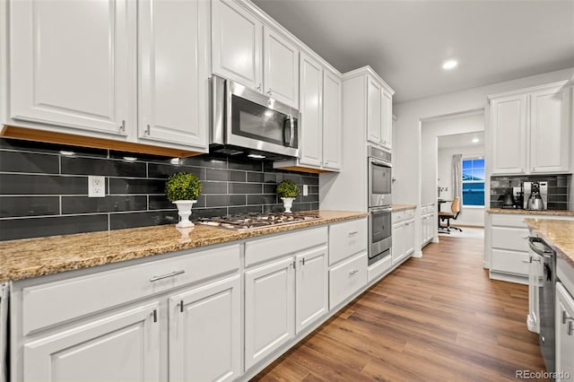 kitchen with appliances with stainless steel finishes, backsplash, white cabinetry, and light wood-style flooring