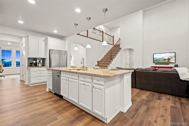 kitchen featuring arched walkways, stainless steel appliances, open floor plan, a sink, and wood finished floors