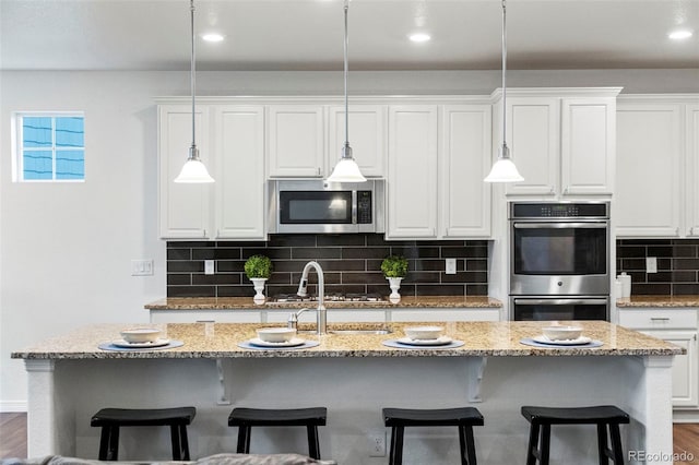 kitchen with appliances with stainless steel finishes, white cabinets, hanging light fixtures, and tasteful backsplash