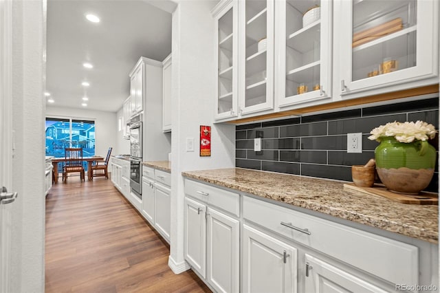 kitchen with light stone counters, wood finished floors, white cabinets, decorative backsplash, and glass insert cabinets