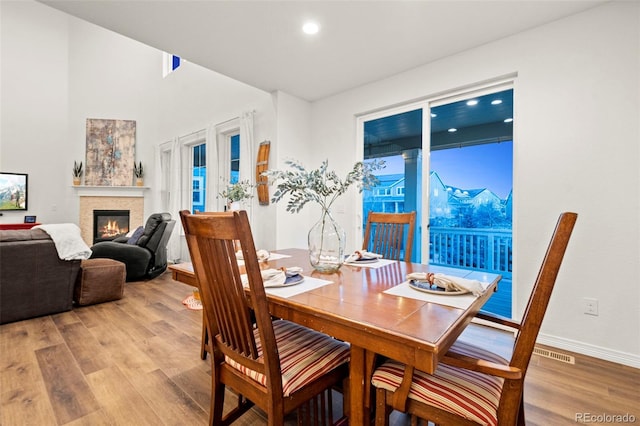 dining space with visible vents, baseboards, a glass covered fireplace, light wood-style flooring, and recessed lighting