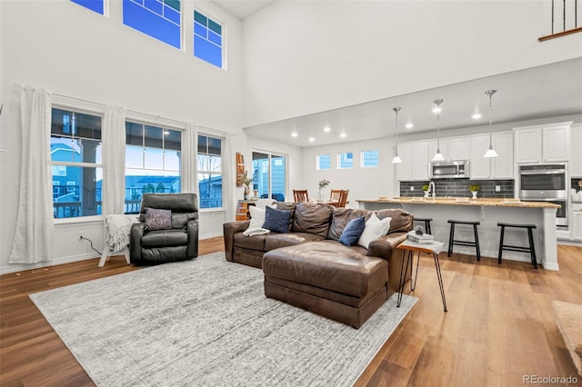 living room with baseboards, a high ceiling, recessed lighting, and light wood-style floors