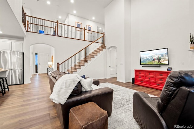 living room featuring light wood-style floors, arched walkways, baseboards, and stairs