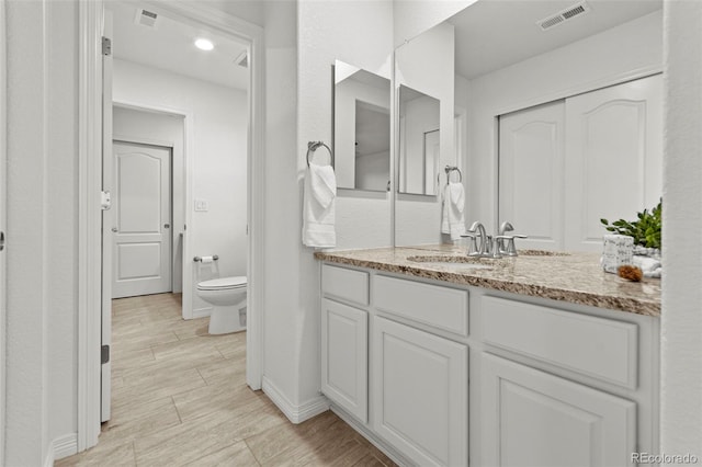 bathroom featuring toilet, wood finish floors, vanity, visible vents, and baseboards