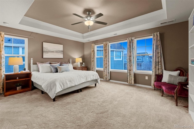 carpeted bedroom featuring ceiling fan, visible vents, baseboards, ornamental molding, and a tray ceiling