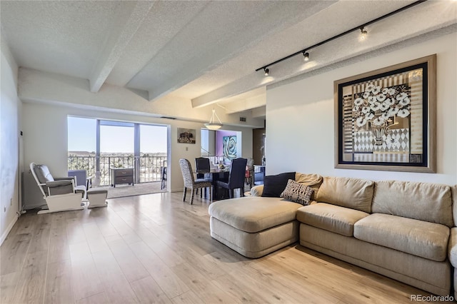 living room with beamed ceiling, a textured ceiling, and light wood-type flooring