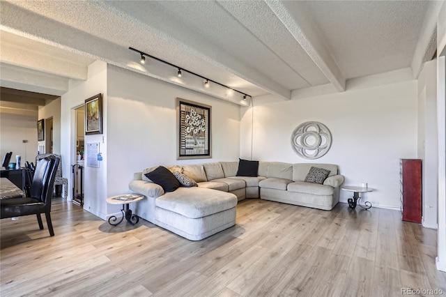 living room with beamed ceiling, rail lighting, a textured ceiling, and light wood-type flooring