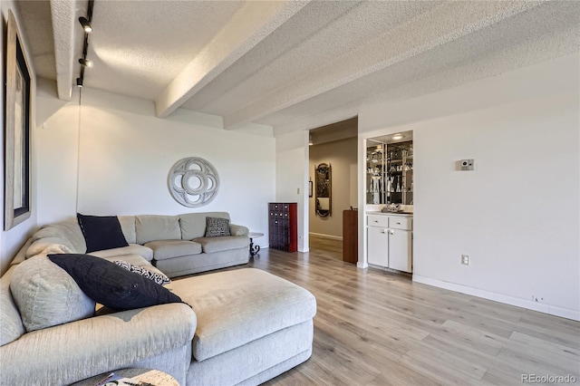 living room featuring beam ceiling, rail lighting, a textured ceiling, and light hardwood / wood-style floors