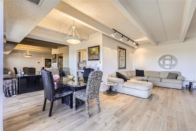 dining area with hardwood / wood-style floors, a textured ceiling, rail lighting, and beamed ceiling