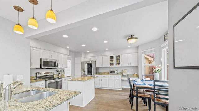 kitchen with light wood finished floors, a sink, white cabinetry, a kitchen island, and stainless steel appliances