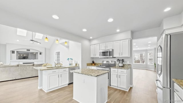 kitchen with a sink, a skylight, light wood finished floors, white cabinetry, and appliances with stainless steel finishes