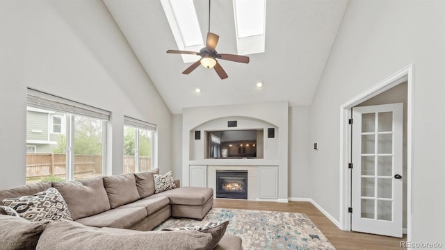 living room with wood finished floors, high vaulted ceiling, a tiled fireplace, baseboards, and ceiling fan