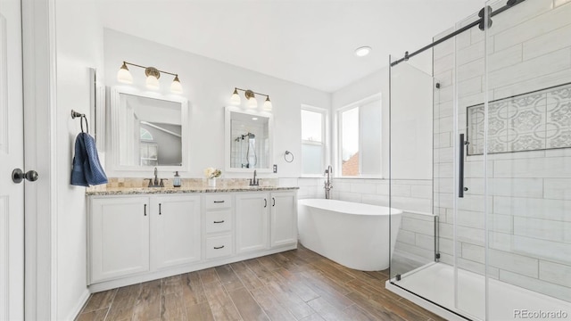 full bath with double vanity, wood finished floors, a sink, a freestanding bath, and a shower stall